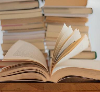 En oppslått bok liggende på et bort, med en stabel av bøker i bakgrunnen.