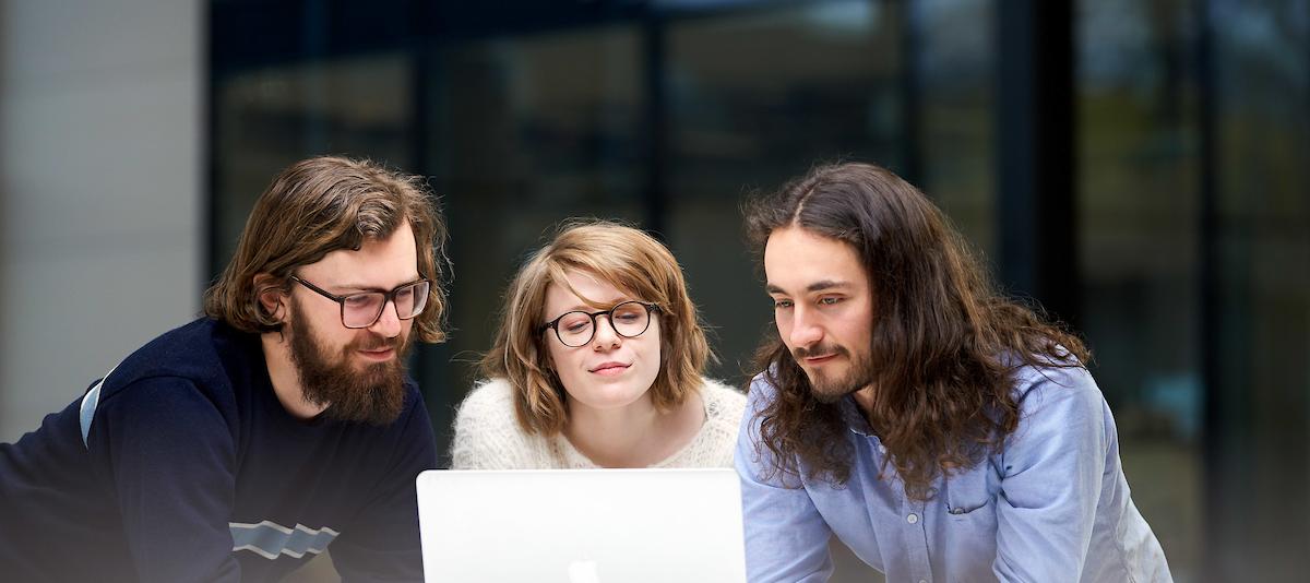 Tre studenter ser på en laptop sammen.