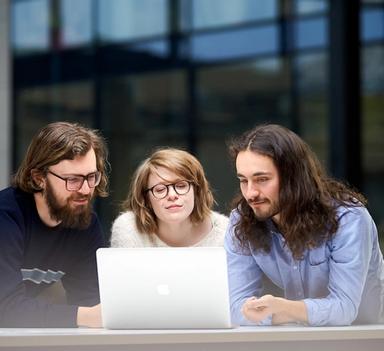 Tre studenter ser på en laptop sammen.