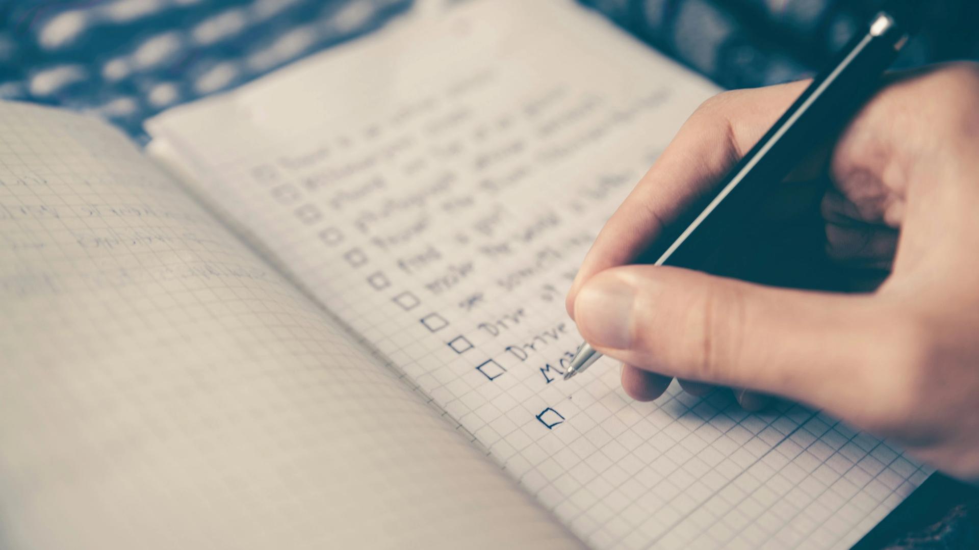 An open notebook with points written down on one page and a hand with a pen.