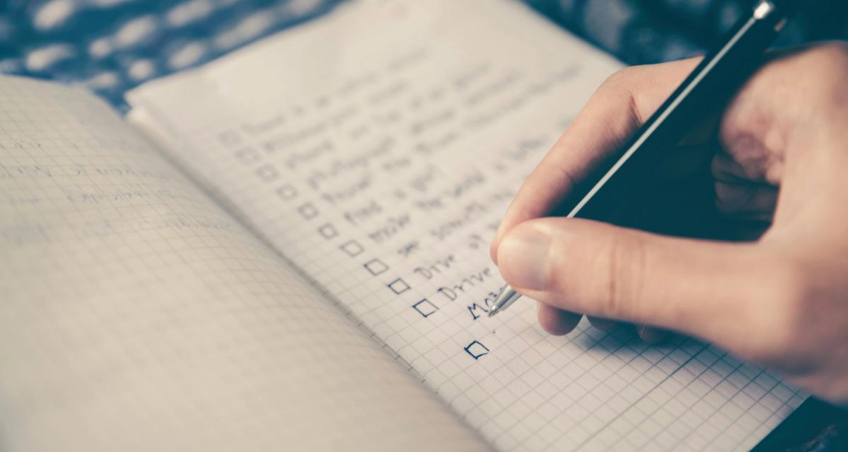 An open notebook with points written down on one page and a hand with a pen.
