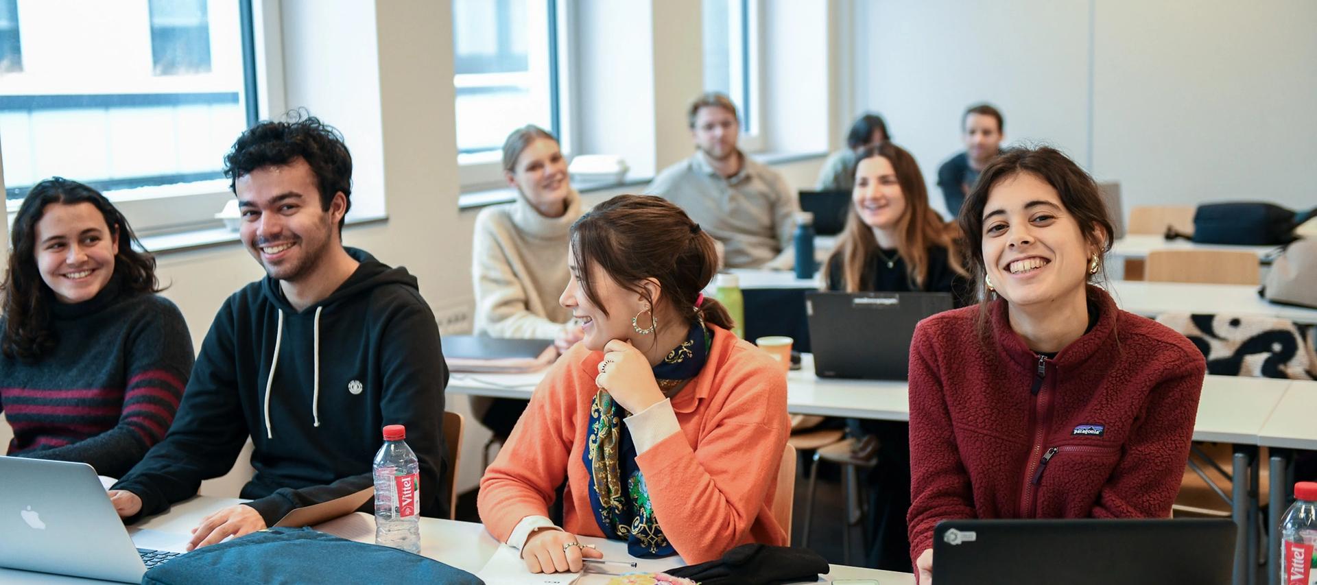 fire studenter sitter på første rad, jenten til høyre ser rett inn i kameraet.