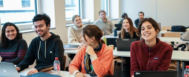 fire studenter sitter på første rad, jenten til høyre ser rett inn i kameraet.