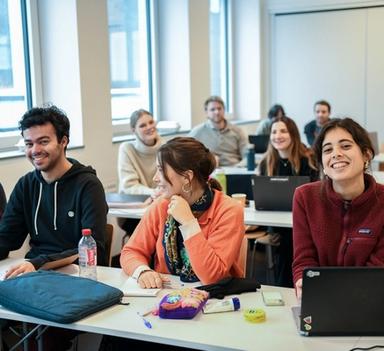 fire studenter sitter på første rad, jenten til høyre ser rett inn i kameraet.