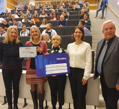 Tre kvinner, en mann og en gutt holder opp et diplom og en gavekort foran et fullsatt auditorium.