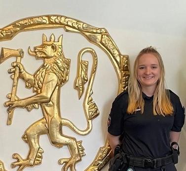 To menn og en kvinne står foran riksvåpenet. Smiler mot kamera.