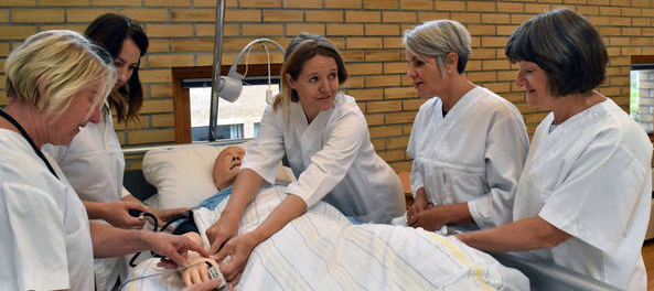Fem sykepleier står rundt en pasientseng.