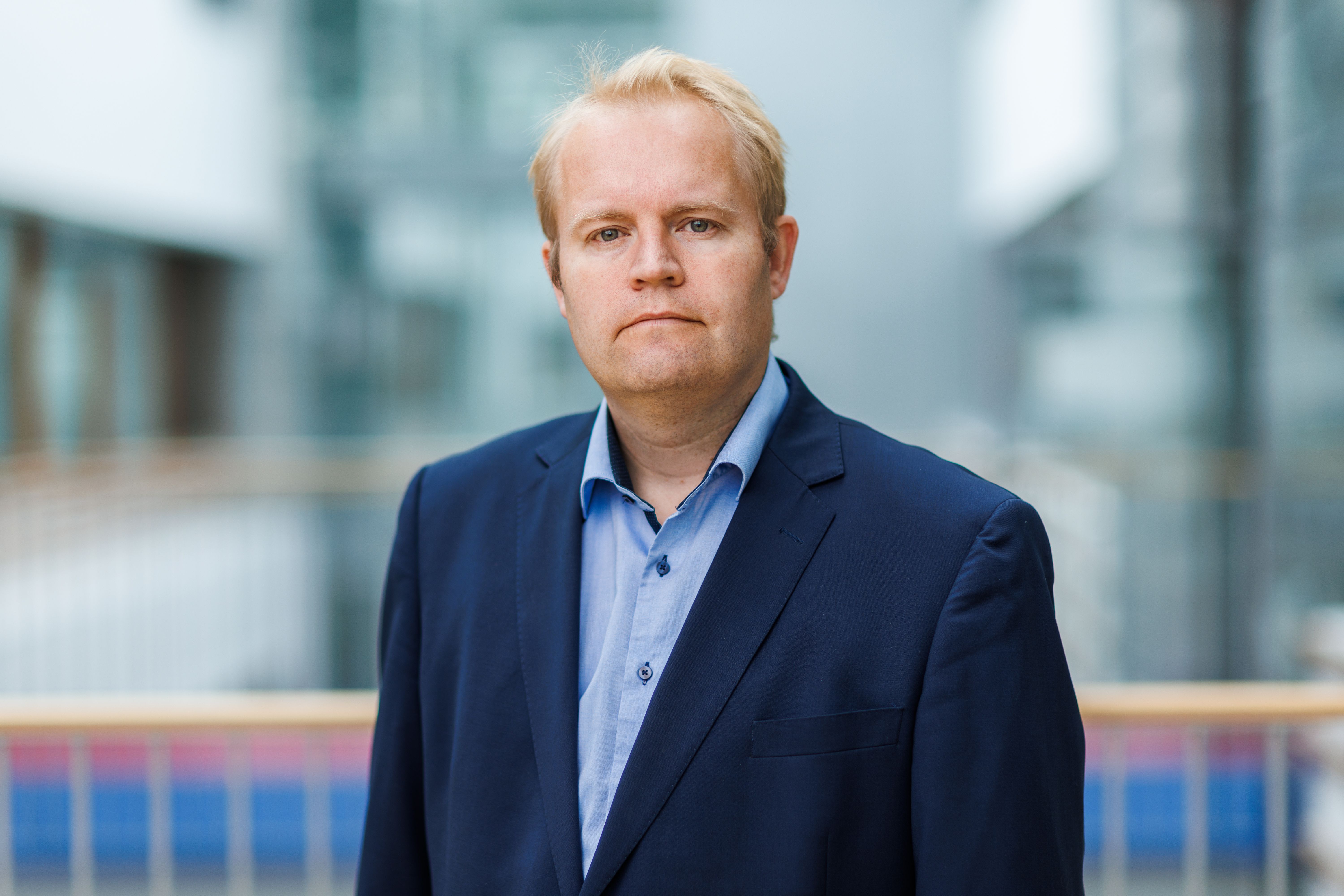 Lars Erling Olsen står i et lyst innemiljø og ser mot kamera. Han har på seg blå dressjakke og lyseblå skjorte.