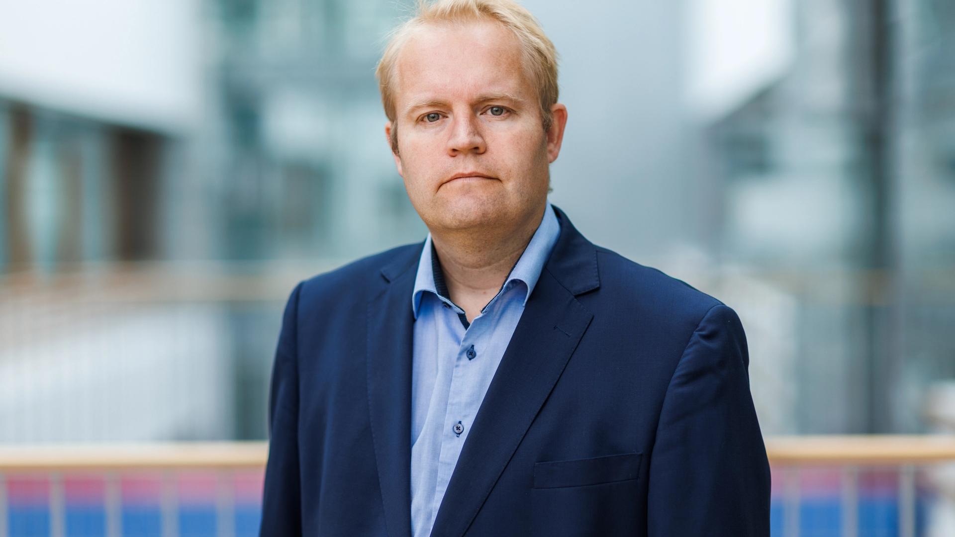 Lars Erling Olsen står i et lyst innemiljø og ser mot kamera. Han har på seg blå dressjakke og lyseblå skjorte.