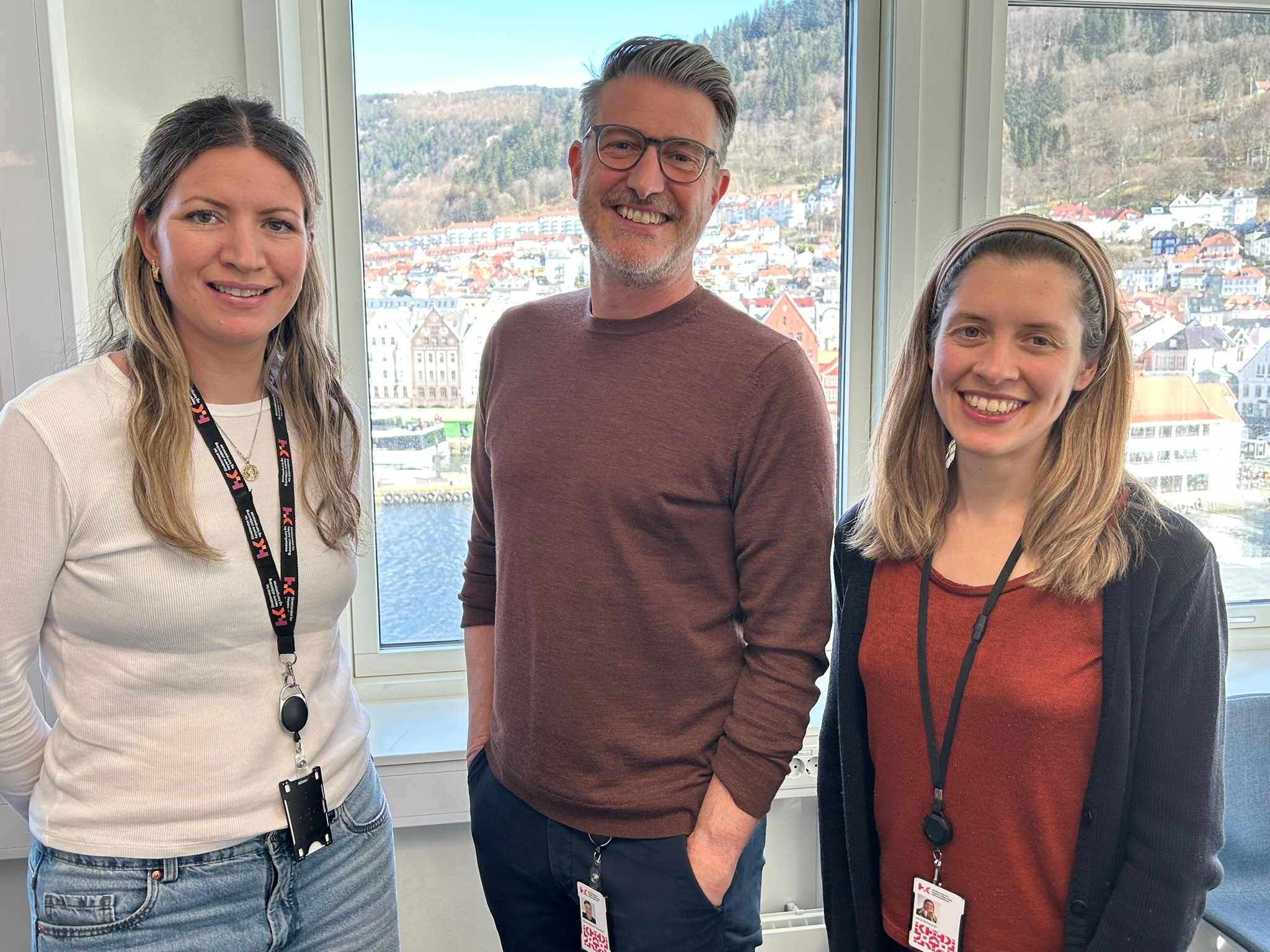 To kvinner og en mann ser smilende mot kameraet