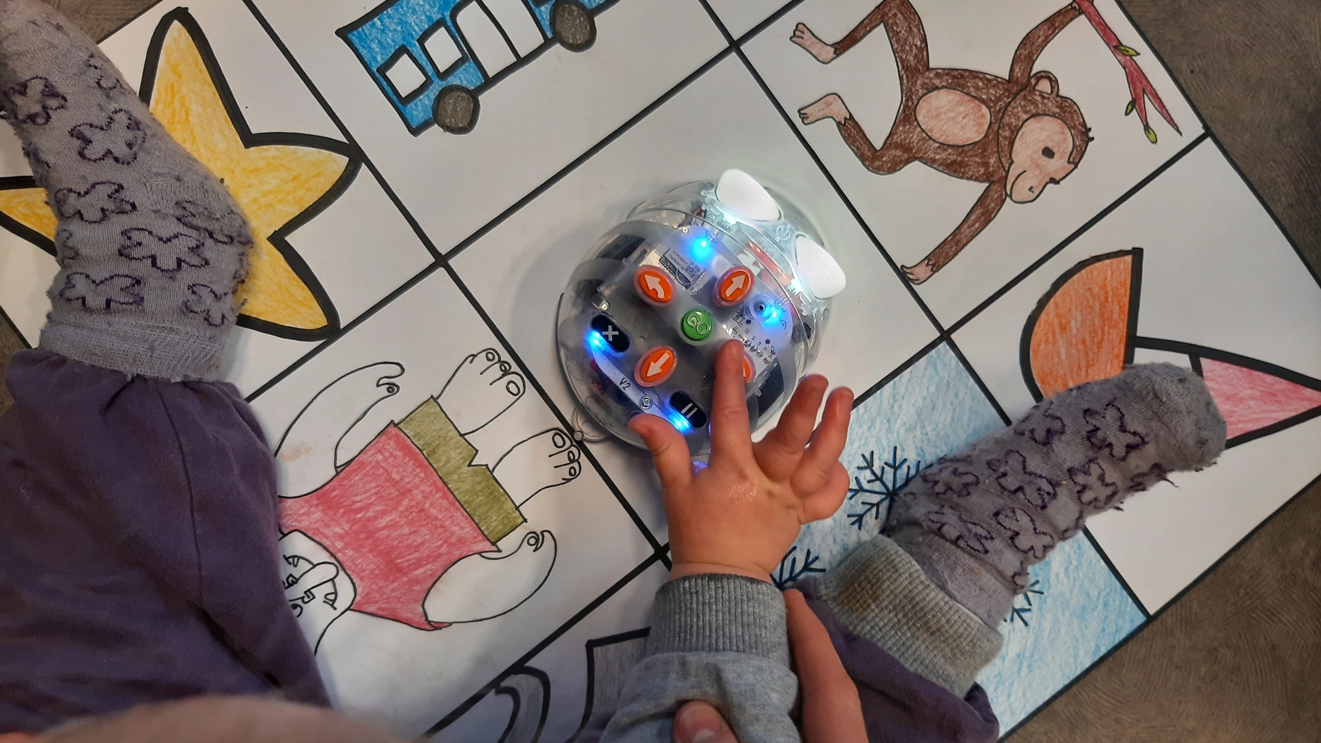 Barn i barnehage holder hånden over en robot som kan kjøres over et tegneark med forskjellige figurer på.