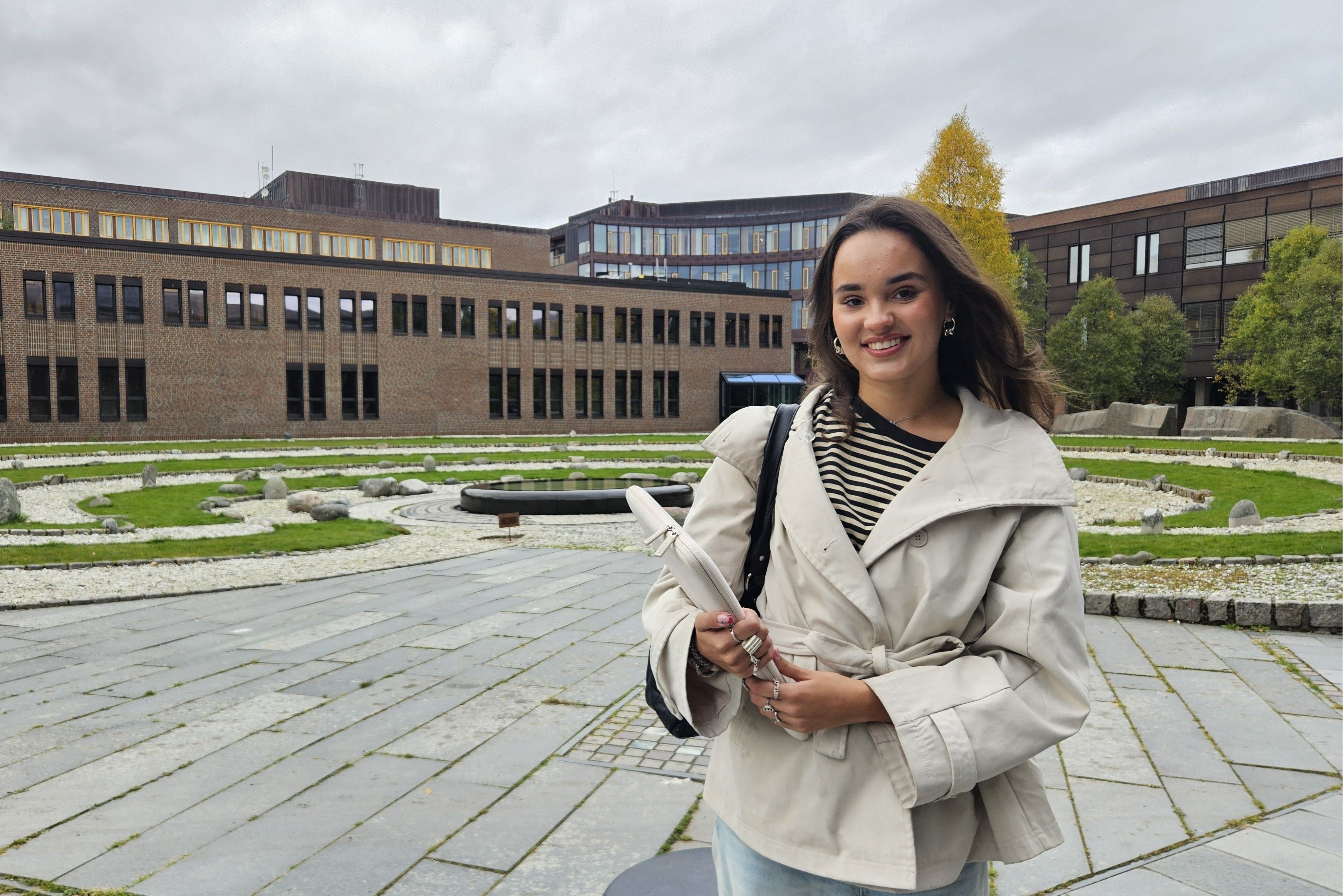 Emmy Wang står utendørs i Tromsø og smiler mot kamera. I bakgrunnen er det bygninger og grøntområder.