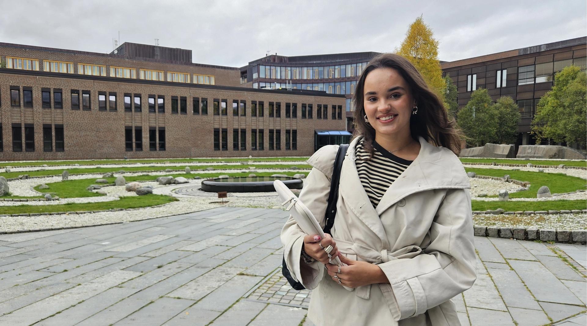 Emmy Wang står utendørs i Tromsø og smiler mot kamera. I bakgrunnen er det bygninger og grøntområder.