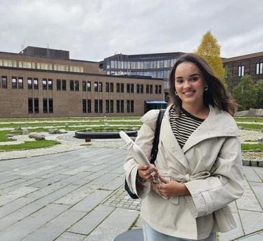 Emmy Wang står utendørs i Tromsø og smiler mot kamera. I bakgrunnen er det bygninger og grøntområder.