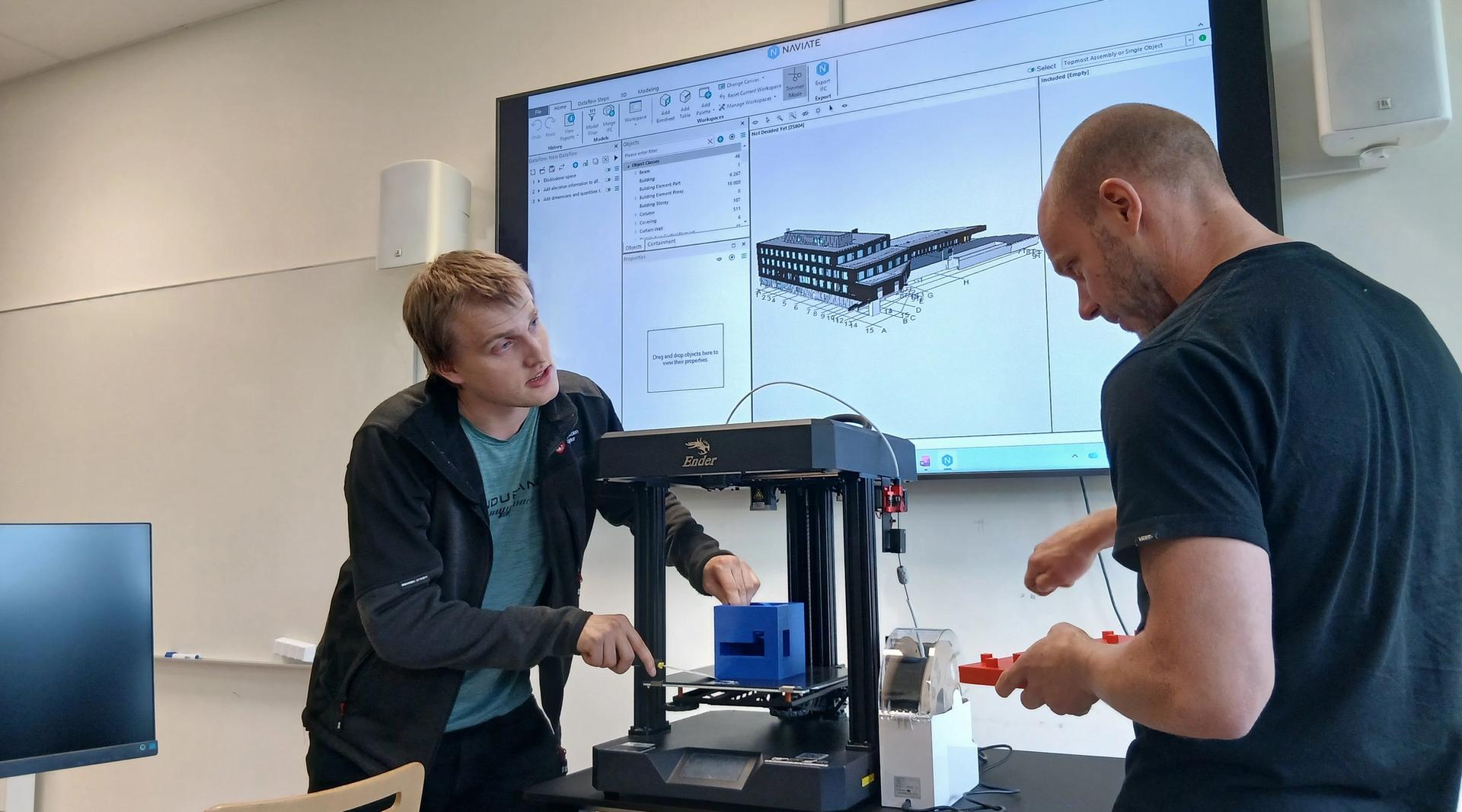 Kristian Spikkeland og Audun Slåtterø demonstrerer 3D-printing i eit laboratorium ved Fagskulen i Agder. Ein digital BIM-modell av eit bygg er synleg på skjermen i bakgrunnen.