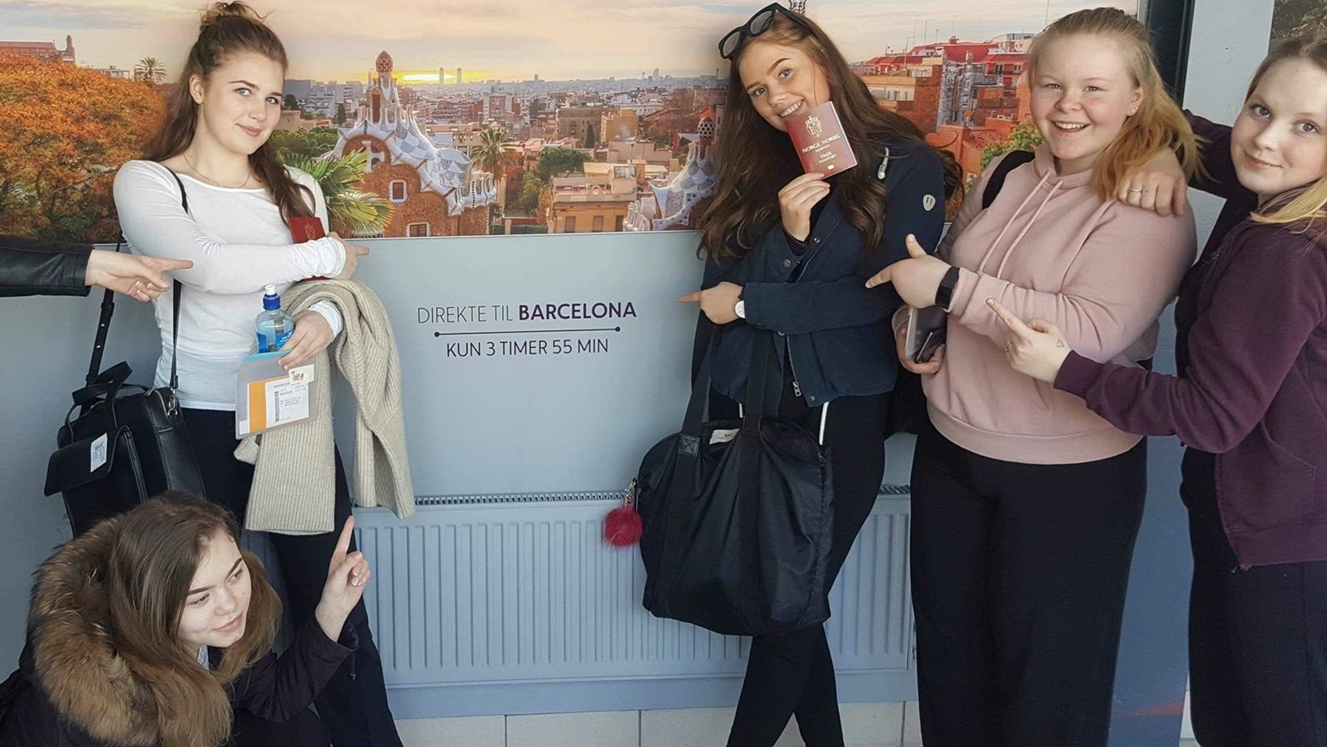 Fire unge jenter står foran en plakat med bilde av Barcelona, mens de peker på teksten "Direkte til Barcelona - Kun 3 timer 55 min".