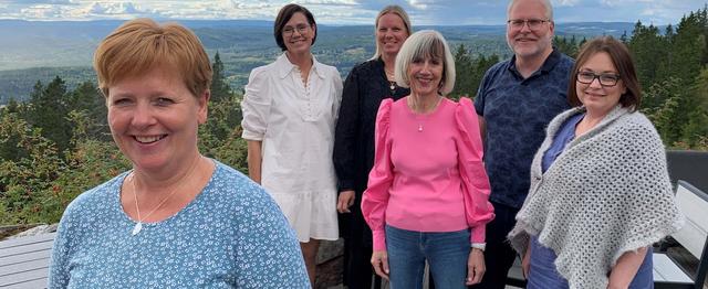 Kvinne i forgrunnen smiler til kamera. I bakgrunnen står fire kvinner og én mann.