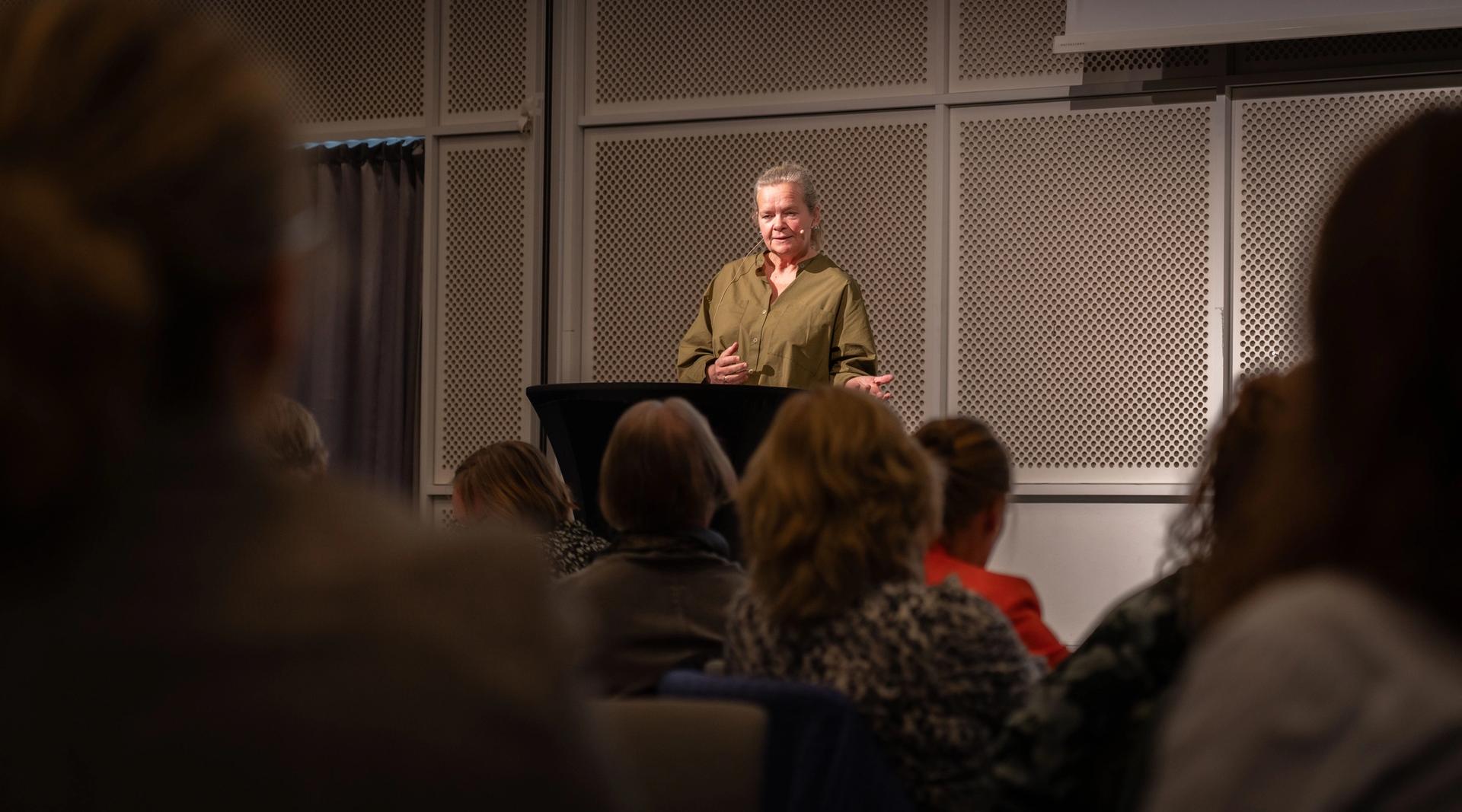 Kvinne holder innlegg foran deltakere på konferanse.