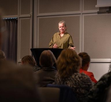 Kvinne holder innlegg foran deltakere på konferanse.