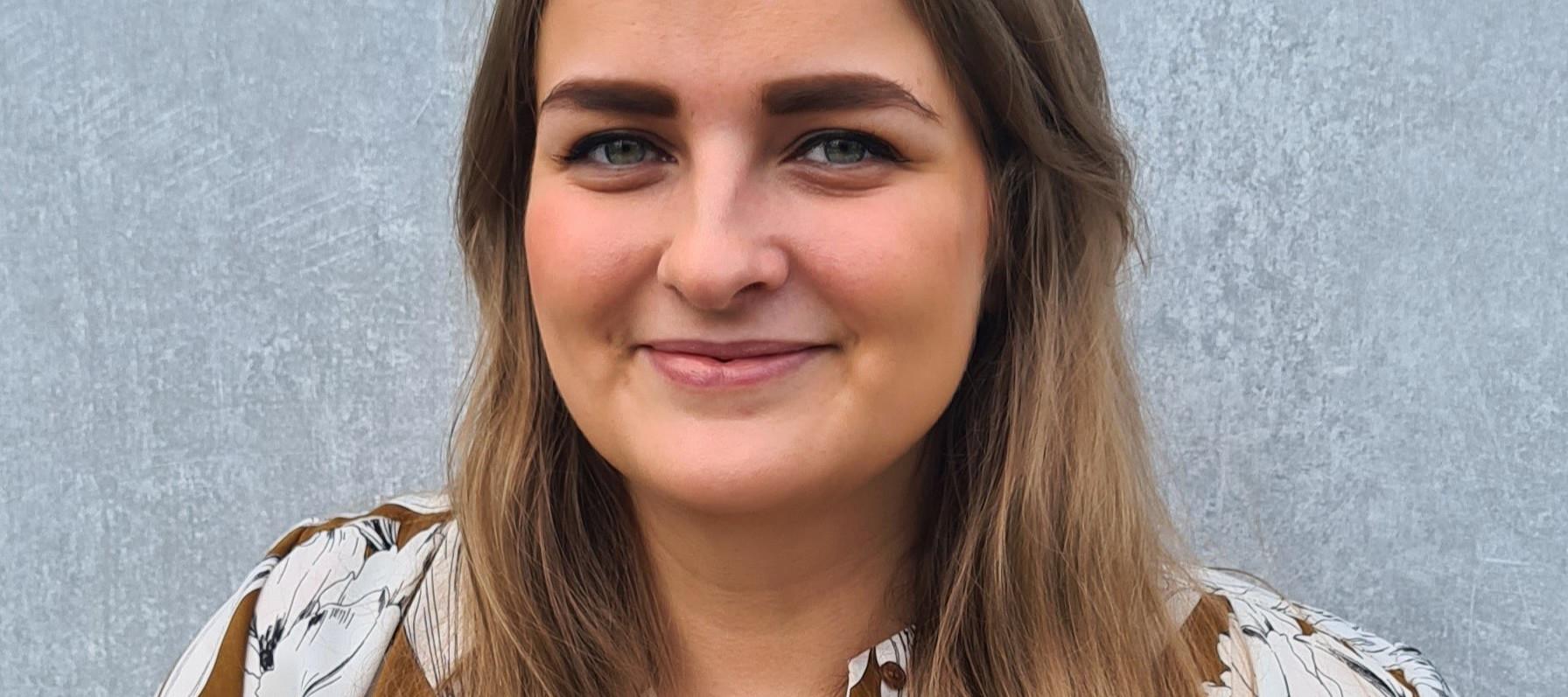 Kvinne i halvprofil ser i kamera og smiler.