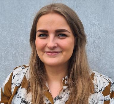 Kvinne i halvprofil ser i kamera og smiler.