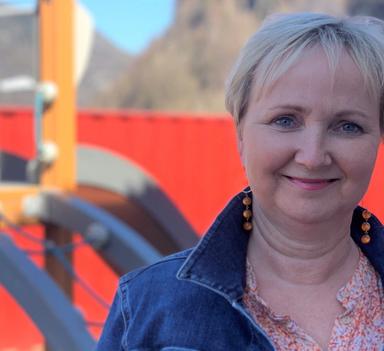 Kvinne står ute og smiler mot kamera. I bakgrunnen kan man skimte uteområdet i en barnehage.