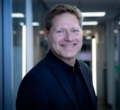 Mann står i korridor i kontorlokale og smiler mot kamera