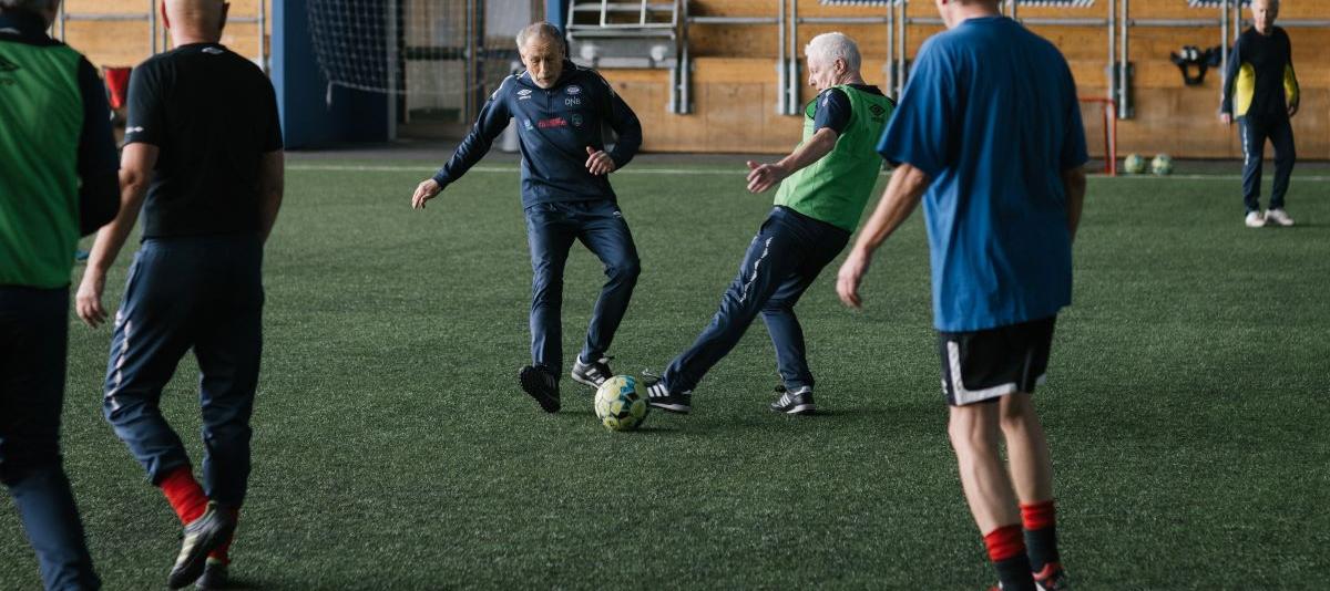 To eldre menn i duell på fotballbanen. Tre andre spiller ser på duellen.