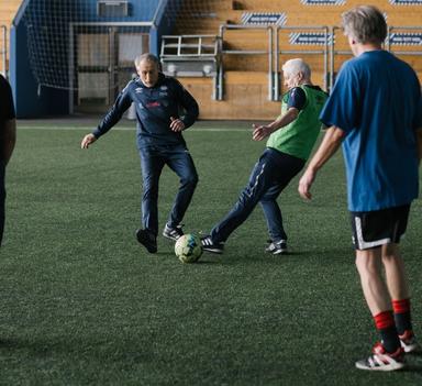 To eldre menn i duell på fotballbanen. Tre andre spiller ser på duellen.