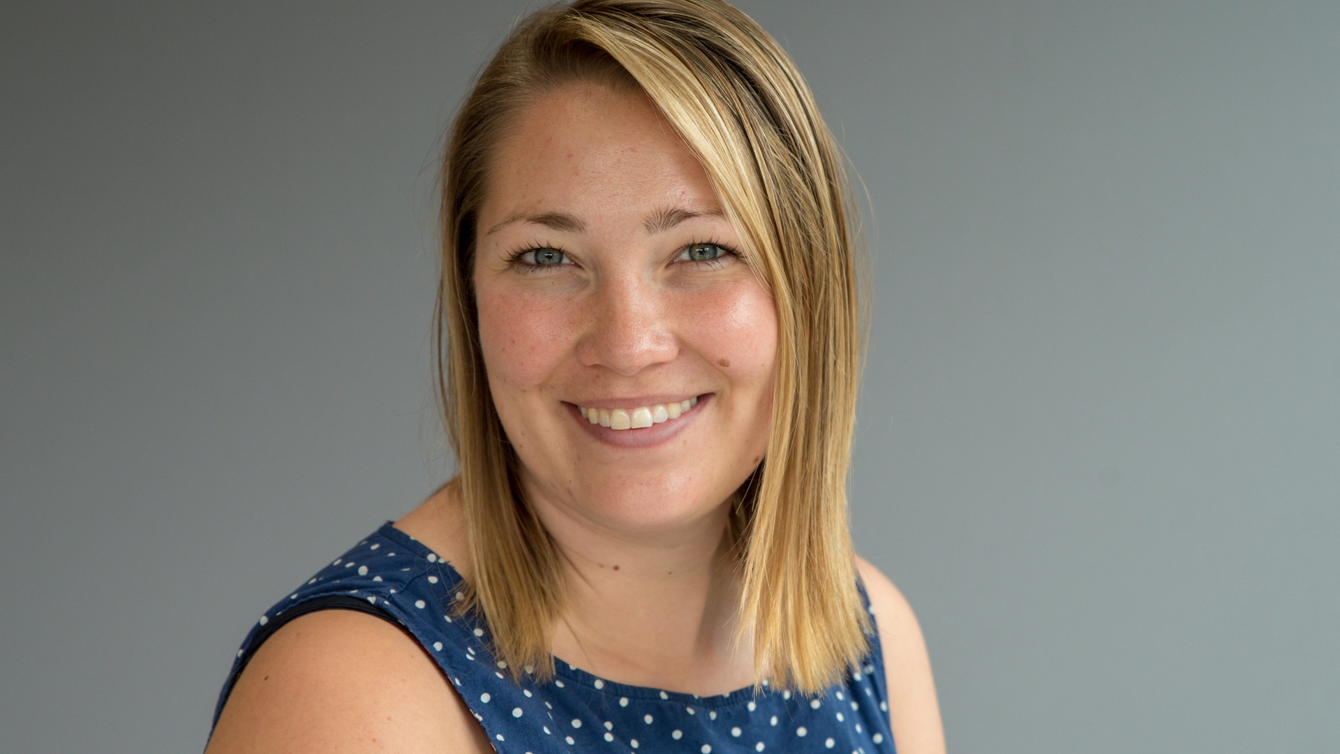 Kvinne i halvprofil smiler og ser i kamera.