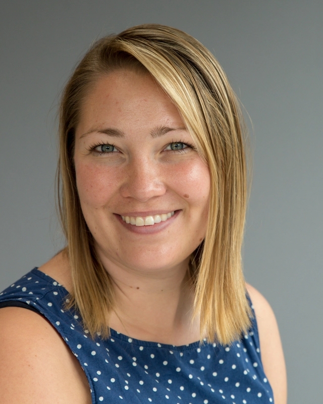 Kvinne i halvprofil smiler og ser i kamera.