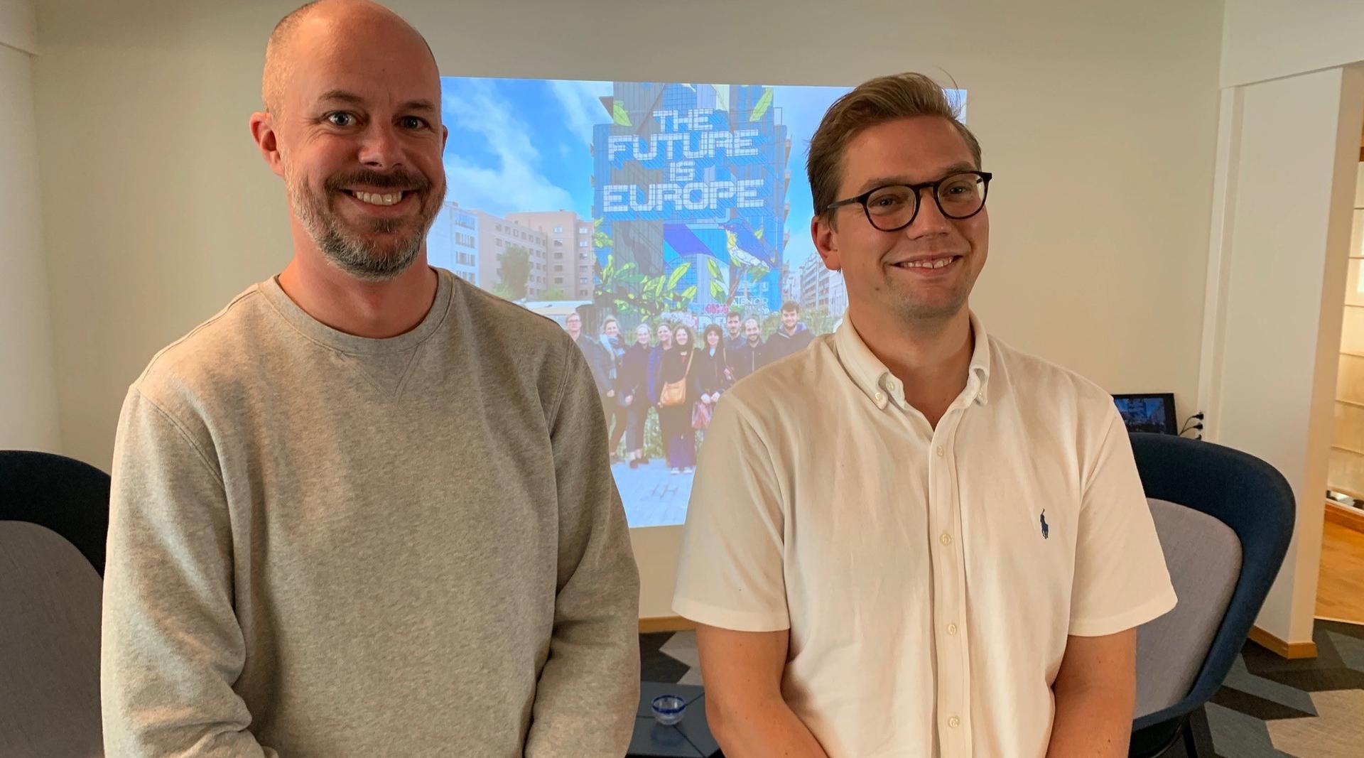 To menn står foran et lerret mens de smiler mot kamera.