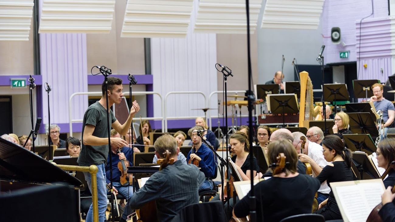 En dirigent står foran et orkester og dirigerer.