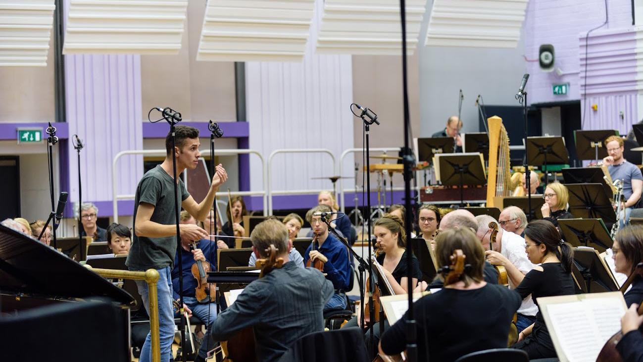 En dirigent står foran et orkester og dirigerer.