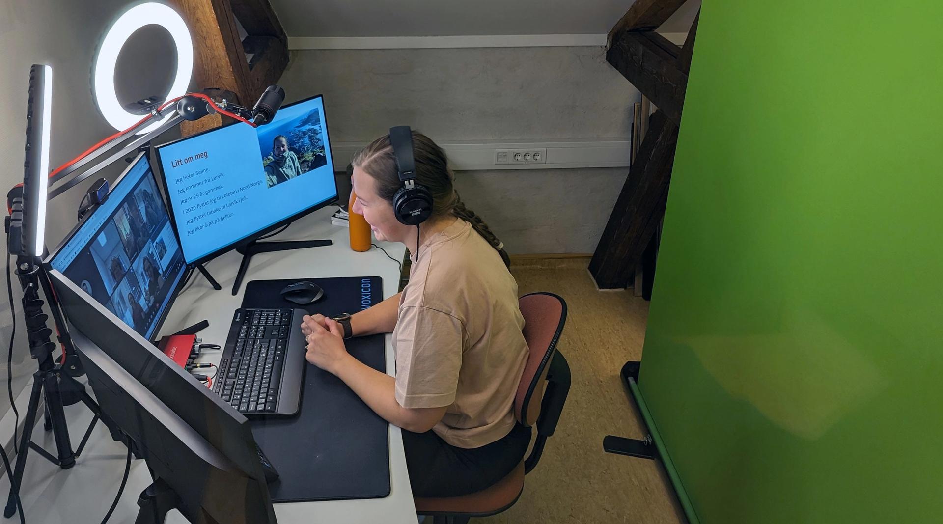 Kvinnelig lærer fjernunderviser fra studio med tre skjermer, ringlys og grønnskjerm.