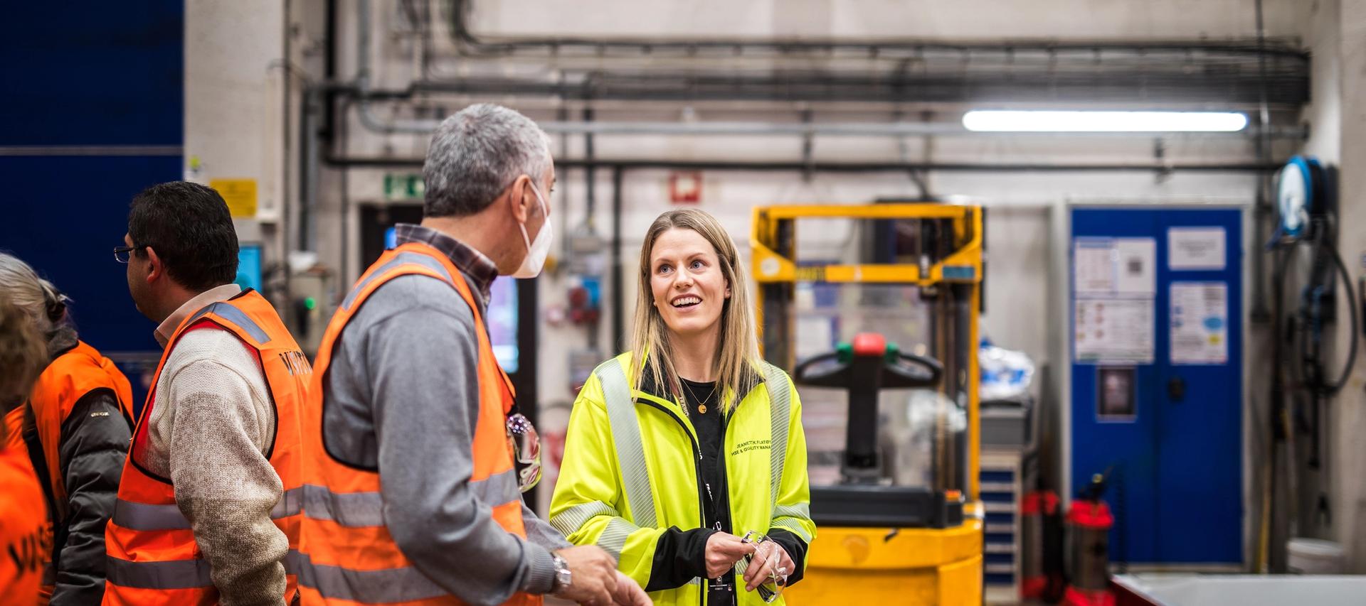 Mann i oransje refleksvest snakker med kvinne med gul arbeidsjakke.