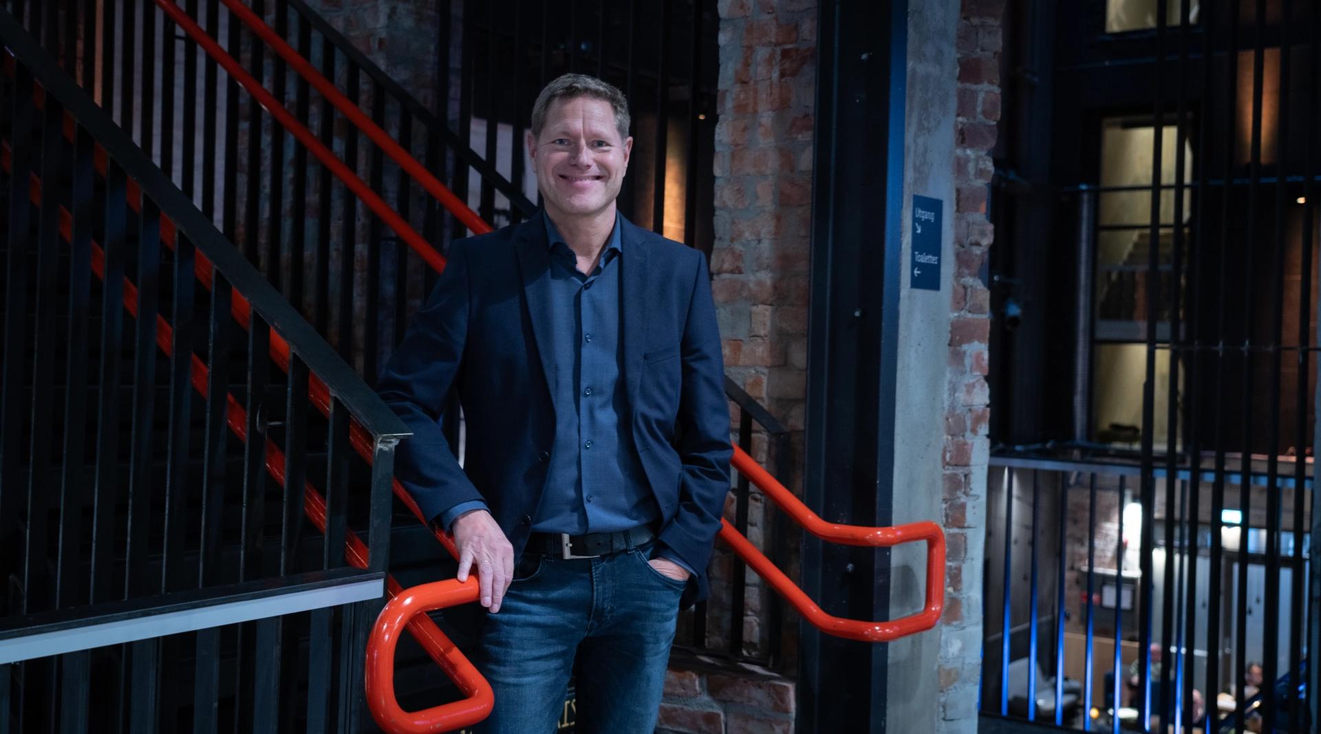 Sveinung Skule fotografert i en trapp med oransje trappegelender.