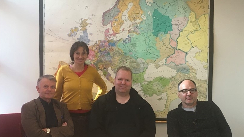 Tre menn sitter foran et verdenskart, mens en kvinne står ved siden av.