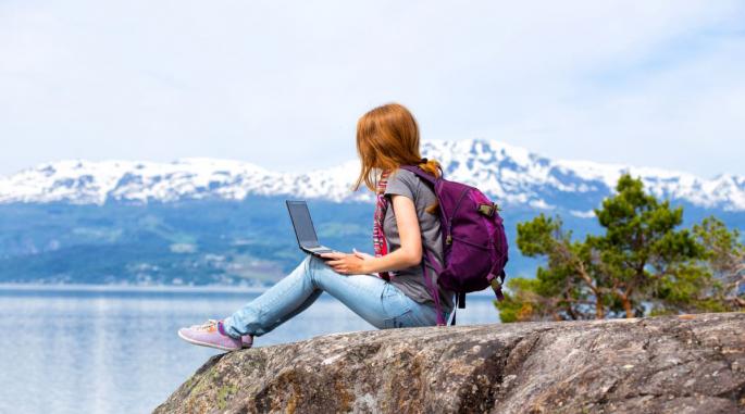 Kvinnelig student med laptop i fanget mens hun ser utover en fjord.