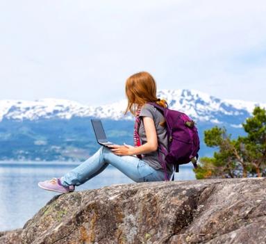 Kvinnelig student med laptop i fanget mens hun ser utover en fjord.