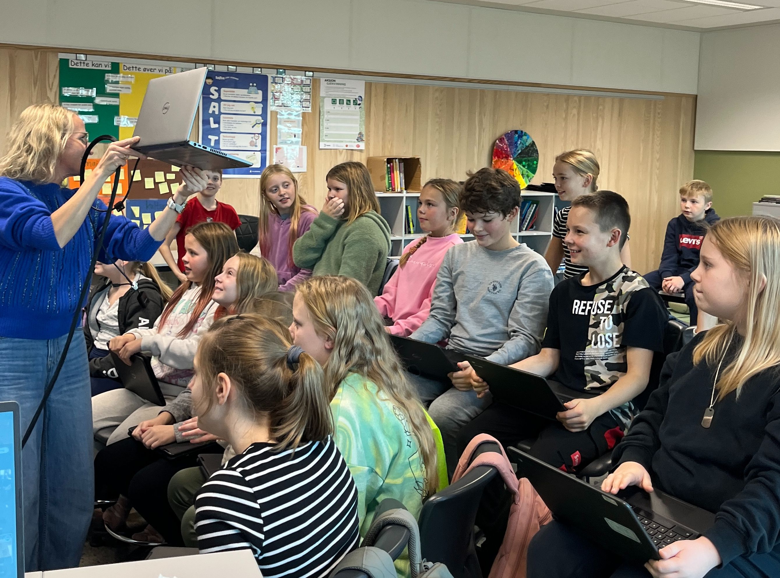 En skoleklasse ser på en lærer som står og holder opp en PC.