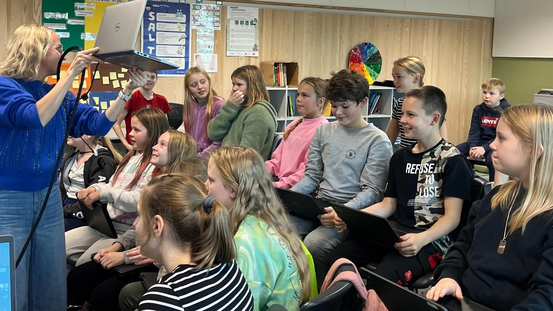 En skoleklasse ser på en lærer som står og holder opp en PC.