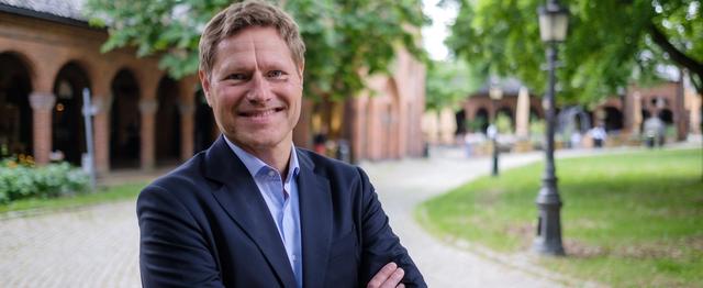 Mann i mørk dress som ser i kamera og smiler
