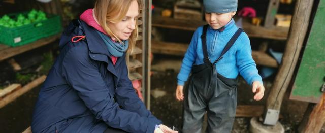 Kvinne sitter på benk utendørs og viser frem et ark til et barn.