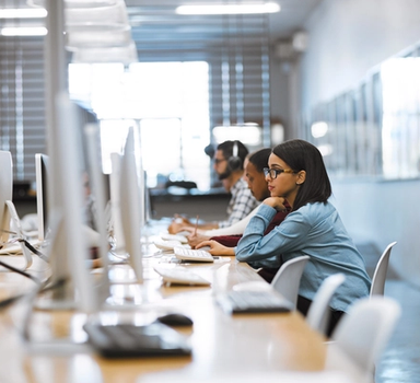 To kvinner og ein mann sit og ser på PC-ar ved eit langbord