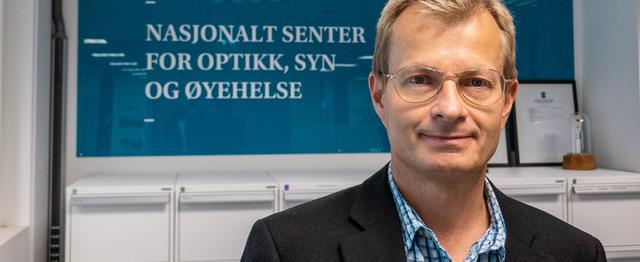 Mann med briller ser mot kamera og smiler.