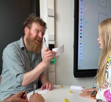 En lærer og en elev å hver sin side av en pult. Læreren holder opp en lapp og smiler.