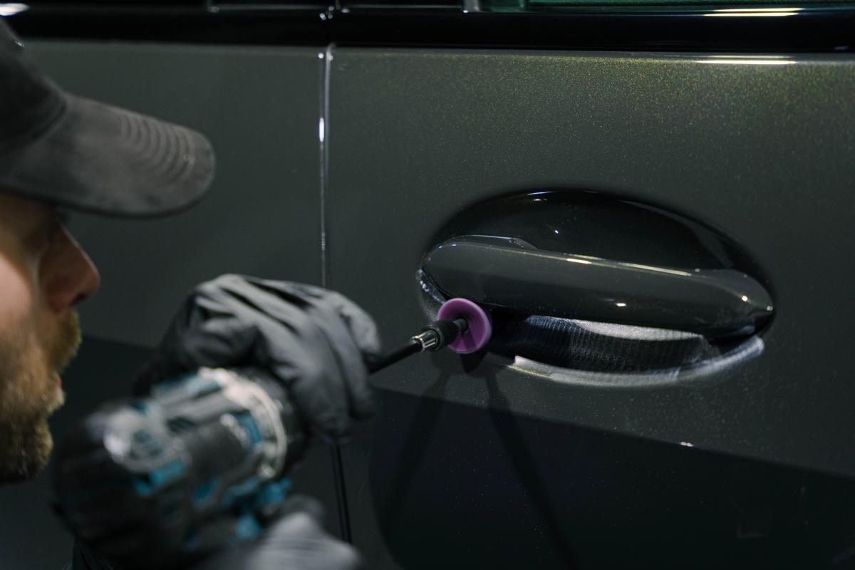 Detailer working precisely around a door handle while preparing paint for protection