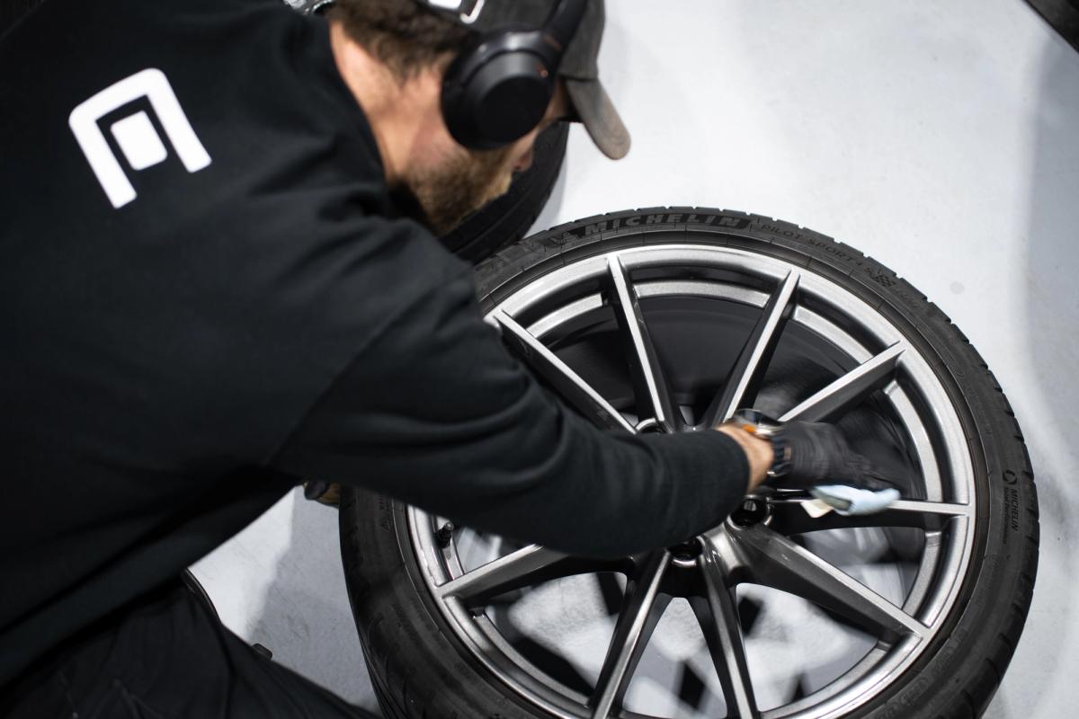 Detailer working on a removed Porsche wheel in the Charlie Detailing studio