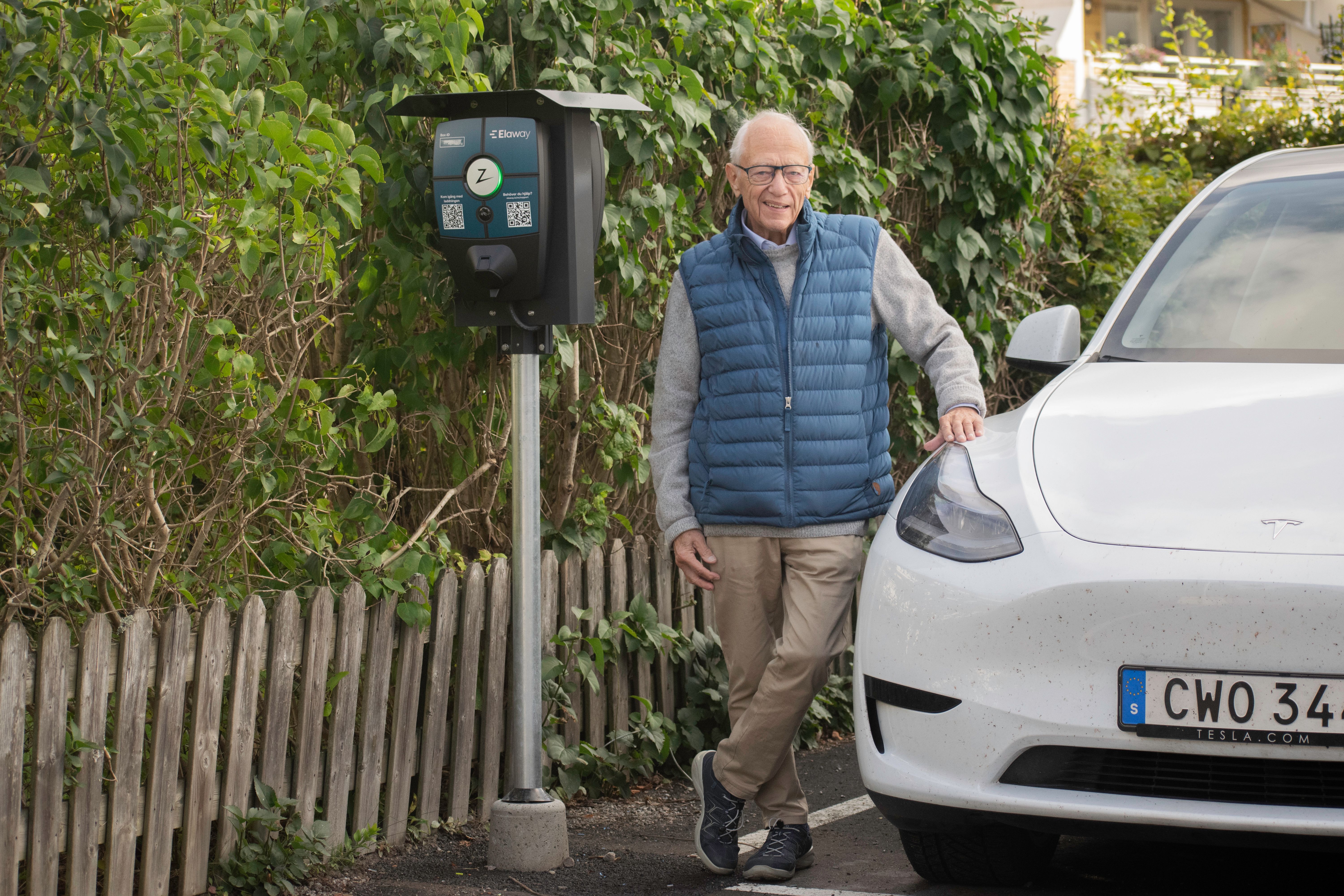 Foto av en man i blå väst som lutar sig mot en vit bil framför en Zaptec-laddstolpe